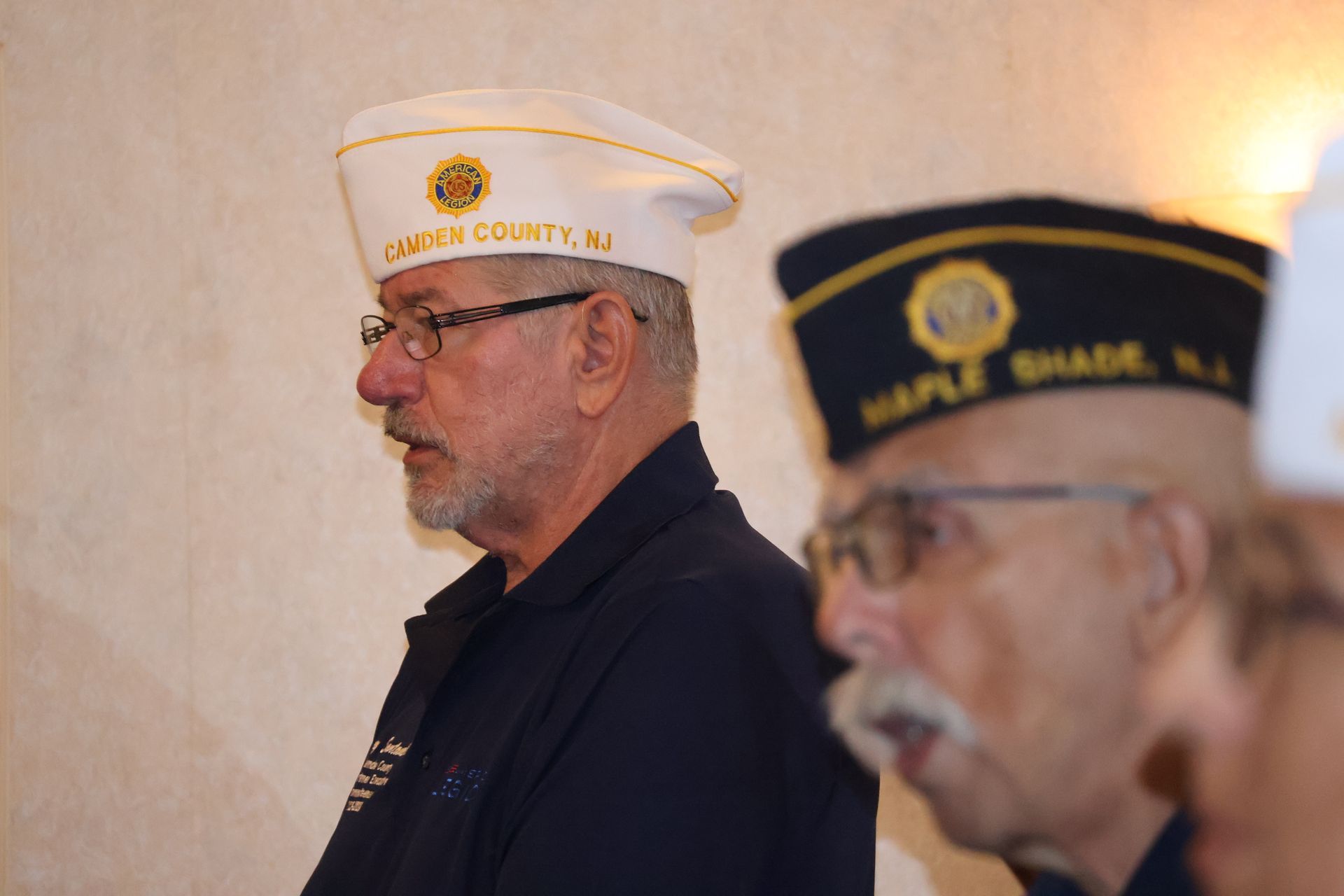 Two men wearing military-style hats; one white with gold emblem, the other navy blue with gold emblem.
