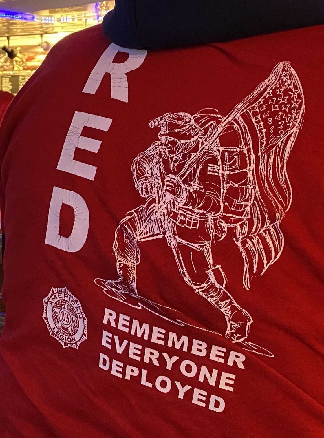 Red t-shirt with white graphic: Soldier carrying American flag, text 