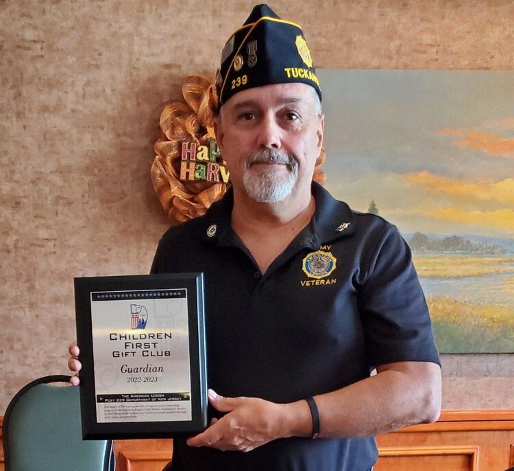 Man in veteran attire holds a plaque from Children First Day Club, smiling indoors.