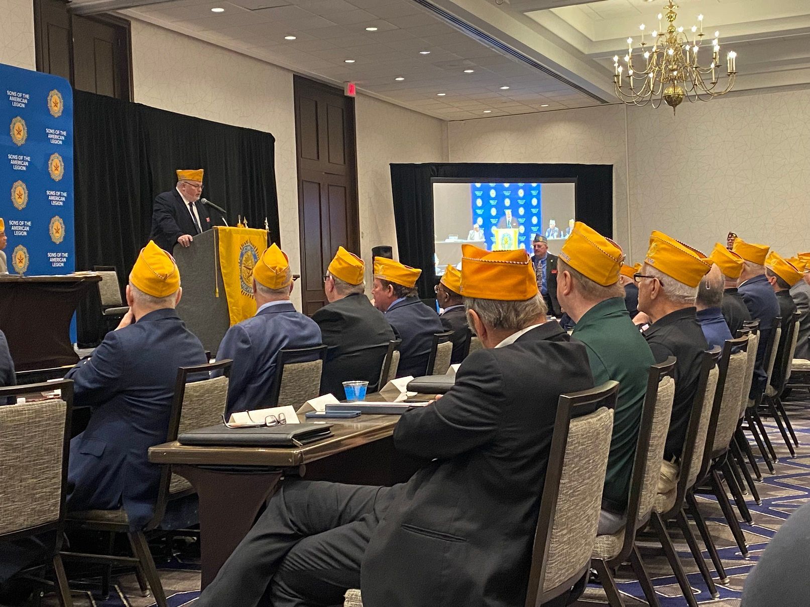 Men in yellow hats listen to a speaker at a conference.