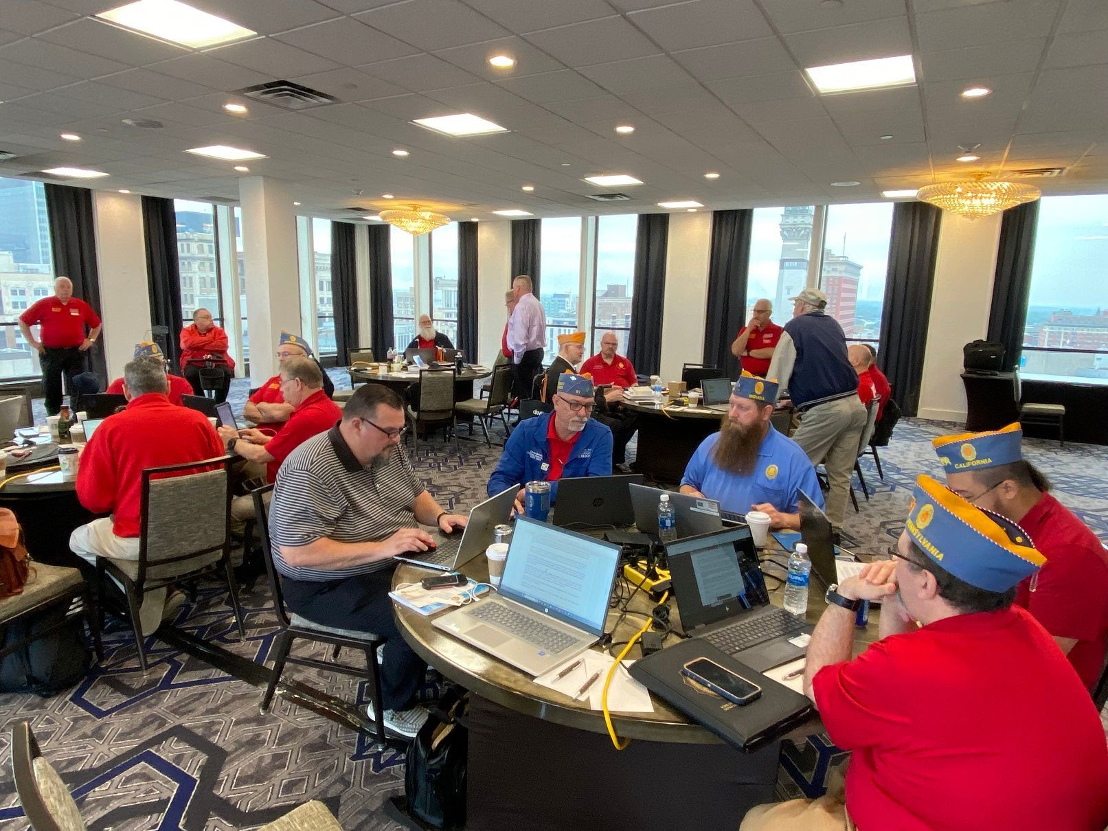 Group of people in red shirts and caps working at tables with laptops in a conference room.