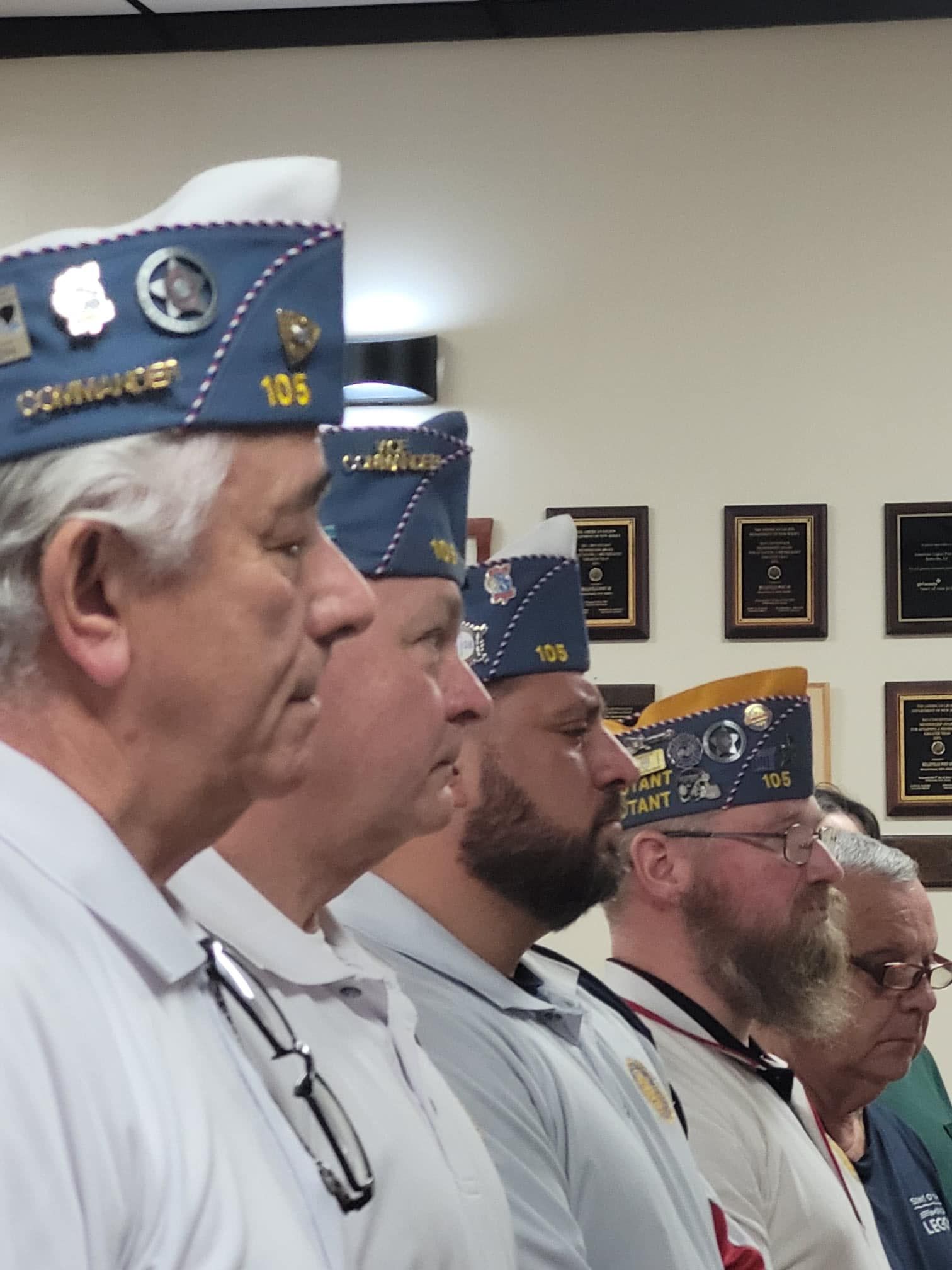 Men in military-style caps and white shirts, standing in a row, likely at a ceremony.