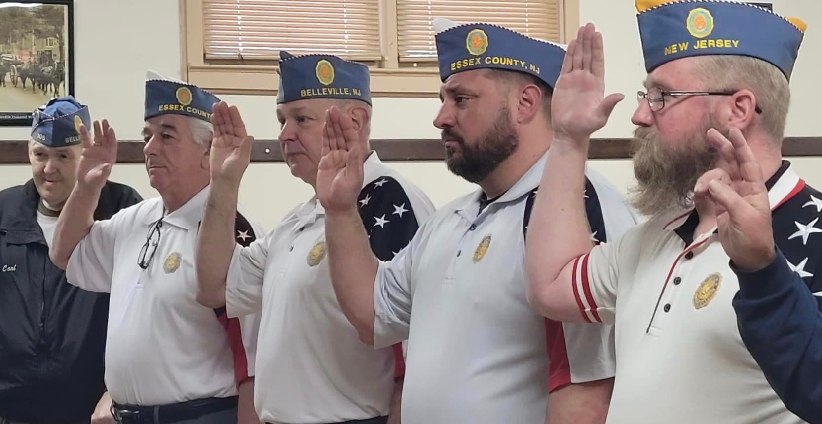 Men in matching hats and shirts taking an oath, raising their right hands indoors.