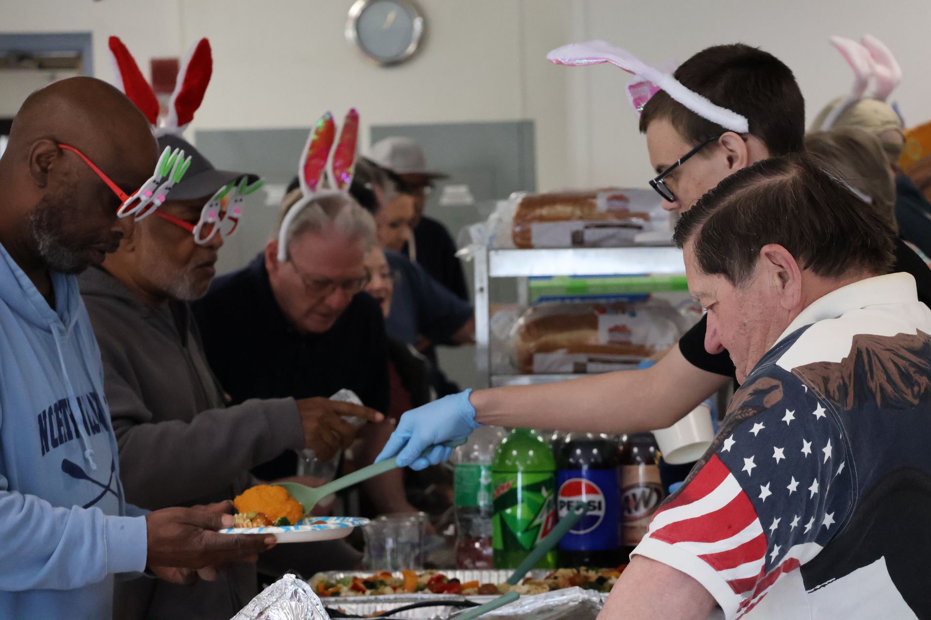 People in holiday headbands serving themselves at a buffet table with drinks and trays