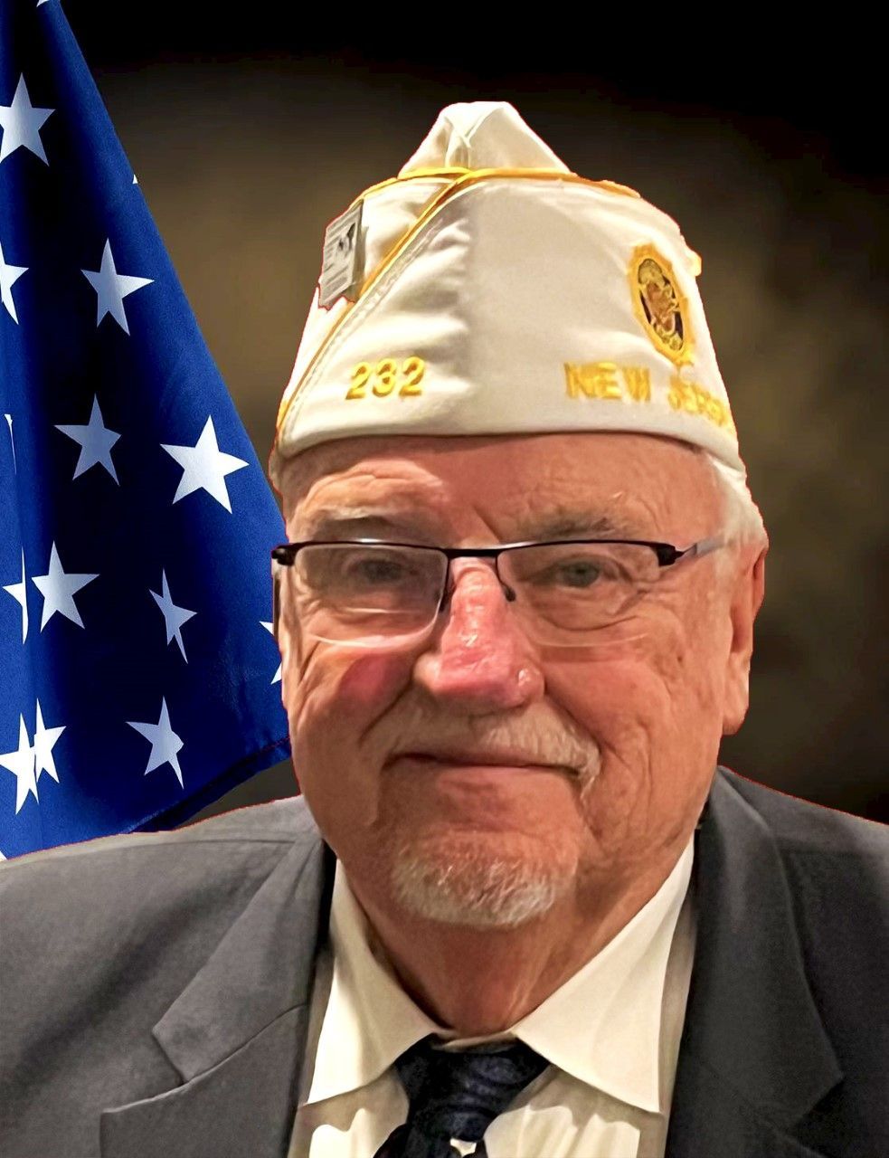 Man wearing glasses and veteran's cap in front of an American flag.