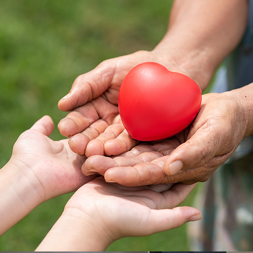 Hands holding a red heart, passing it to another pair of hands.