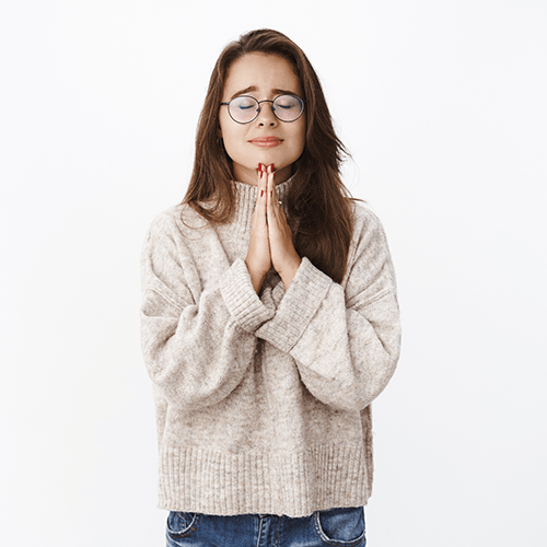 Woman with glasses in a beige sweater, hands clasped in front of her, eyes closed.