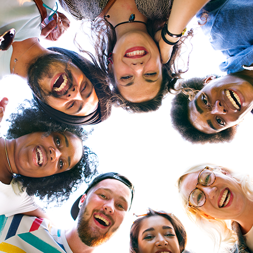 People smiling, looking down, forming a circle. Viewed from below with a bright sky.