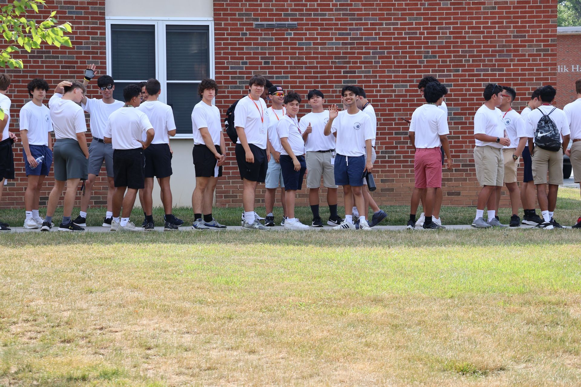 Group of people in white shirts and shorts stand in front of a brick building.