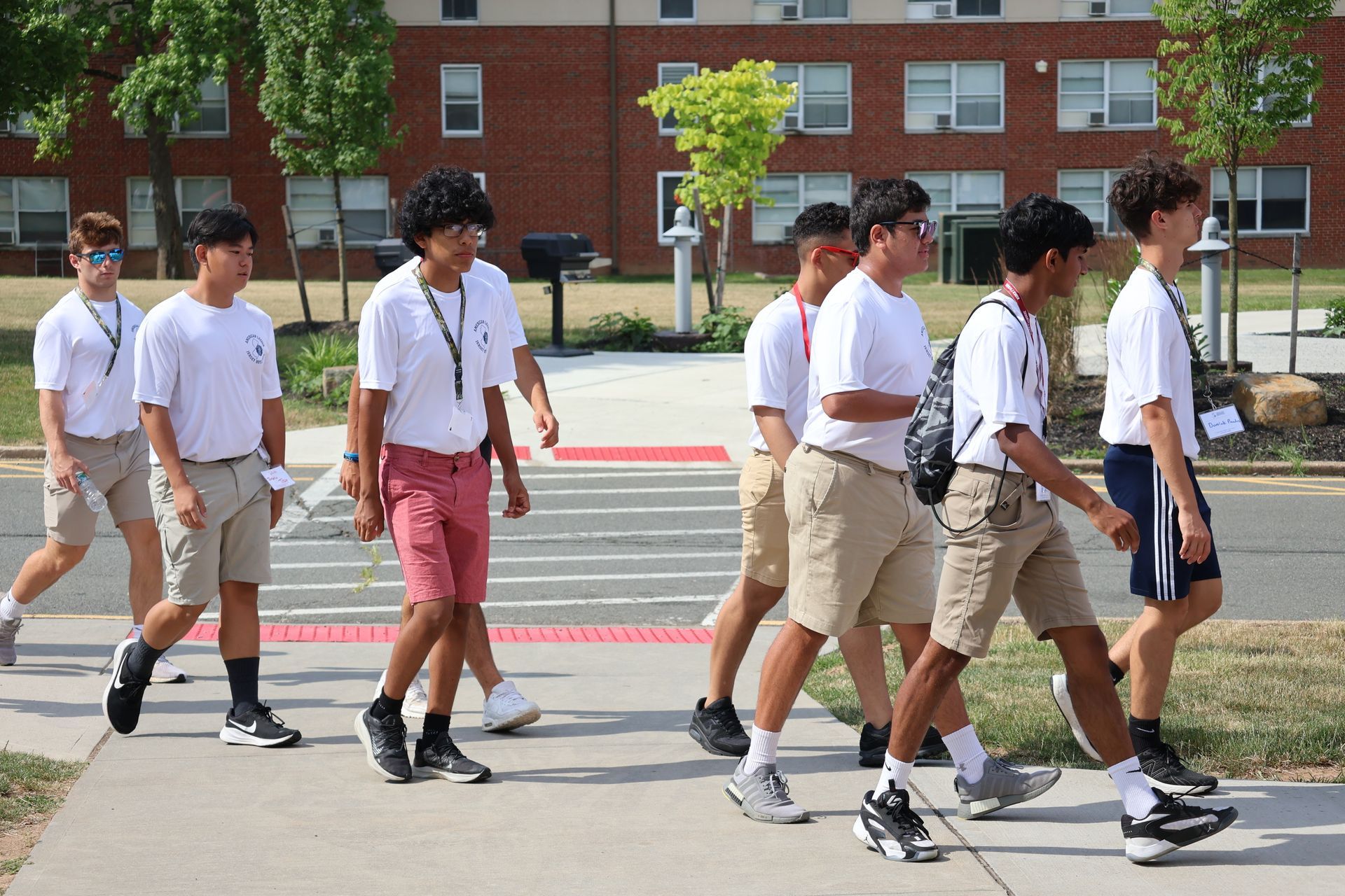 Group of students walking on a sidewalk in front of a brick building on a sunny day.