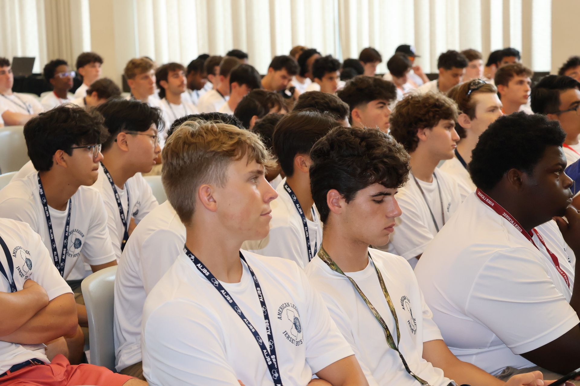 Group of people in white shirts listening attentively in a room.