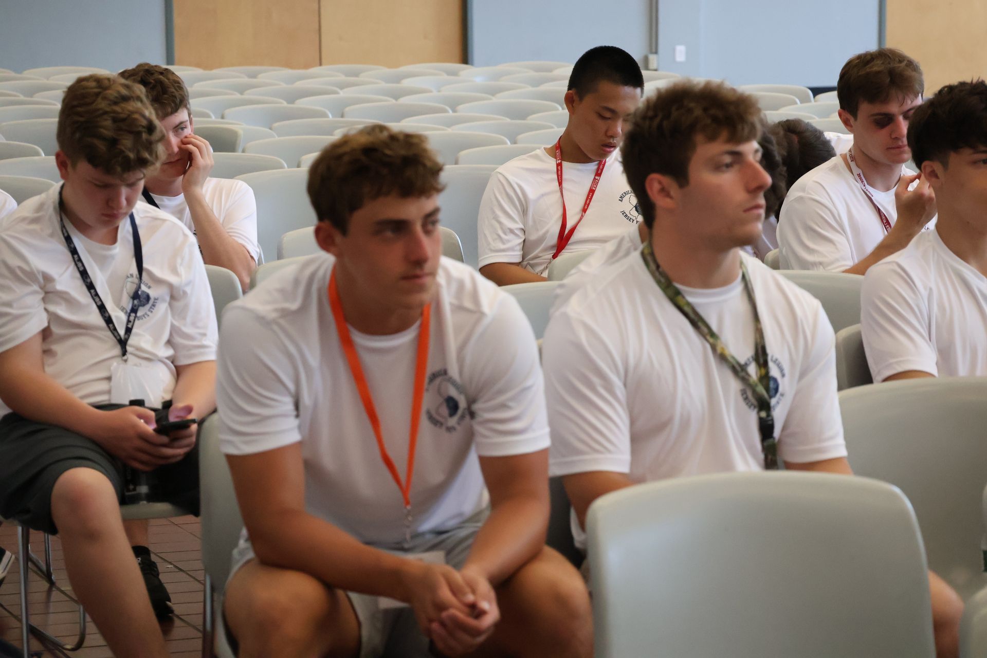 People seated in an auditorium, wearing white shirts and lanyards.