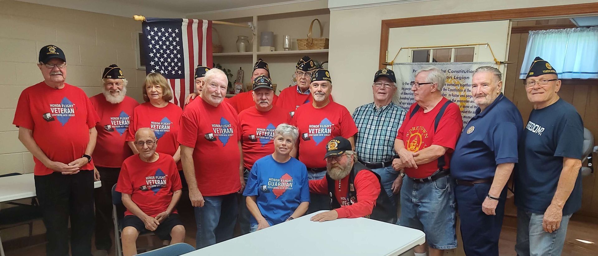 Group of people wearing red shirts and hats in a room with an American flag.