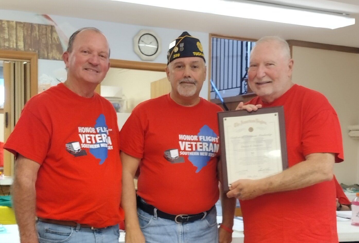 Three men in red shirts with a logo, one holding a framed certificate.