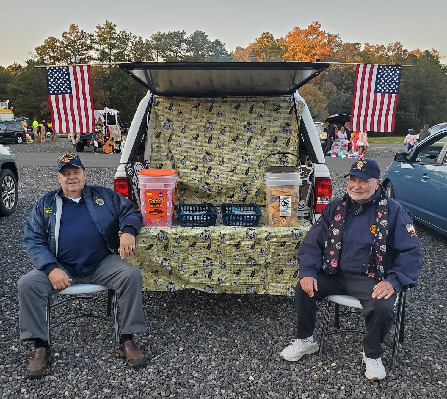 Two men seated in front of a decorated truck tailgate with American flags. Treats are visible.