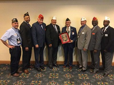 Group of men in suits and hats posing with a plaque in a conference room.