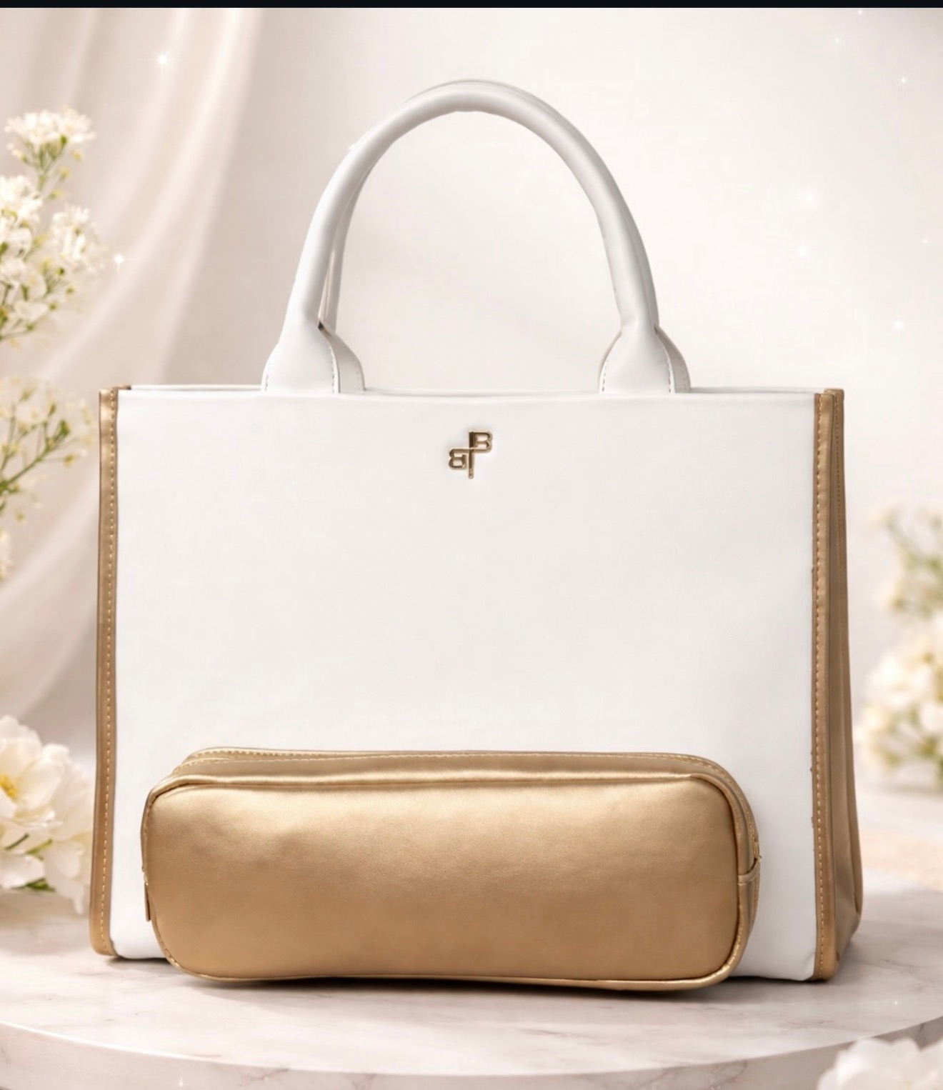 White handbag with gold trim and matching gold zip pouch on a soft floral background