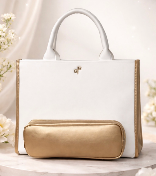 White tote bag with gold trim and a gold pouch on a light floral background