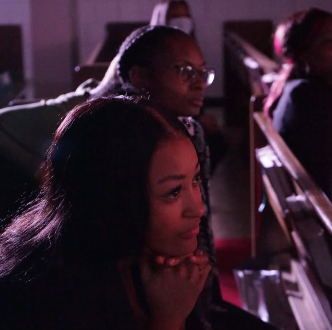 Two people seated in a dimly lit auditorium, watching something off-screen