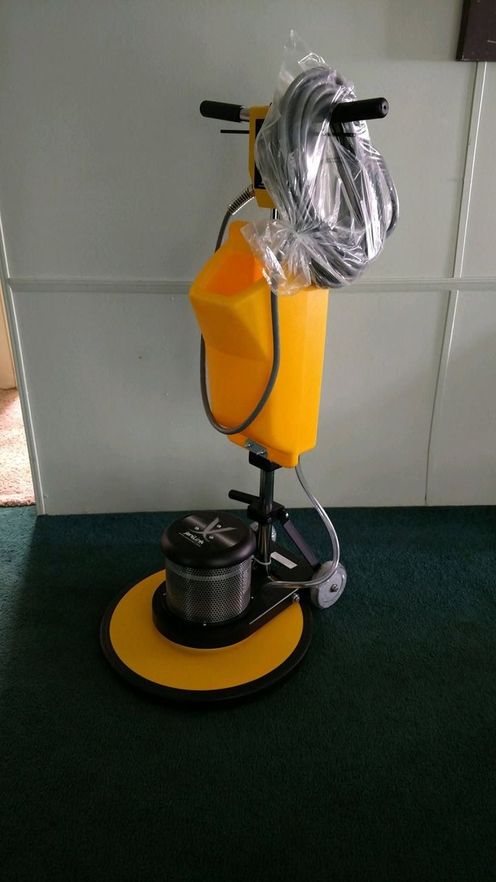 Yellow floor-polishing machine with attached vacuum hose on a green carpeted floor