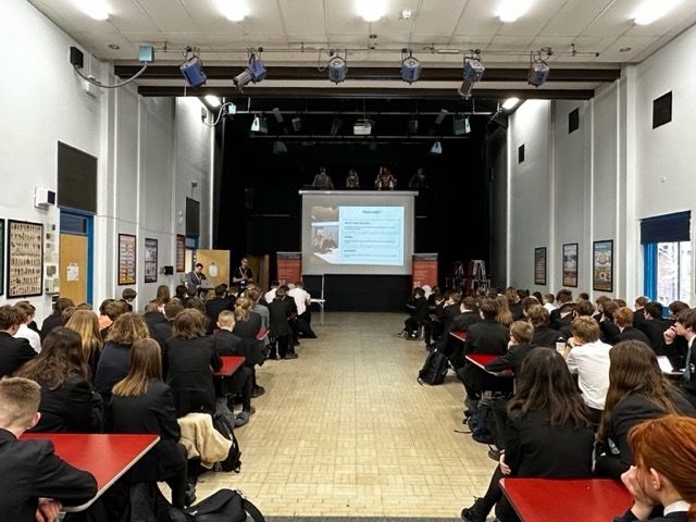 Photograph of a large hall filled with school students and a large projection screen showing CEDIA NextGen Presenation on it