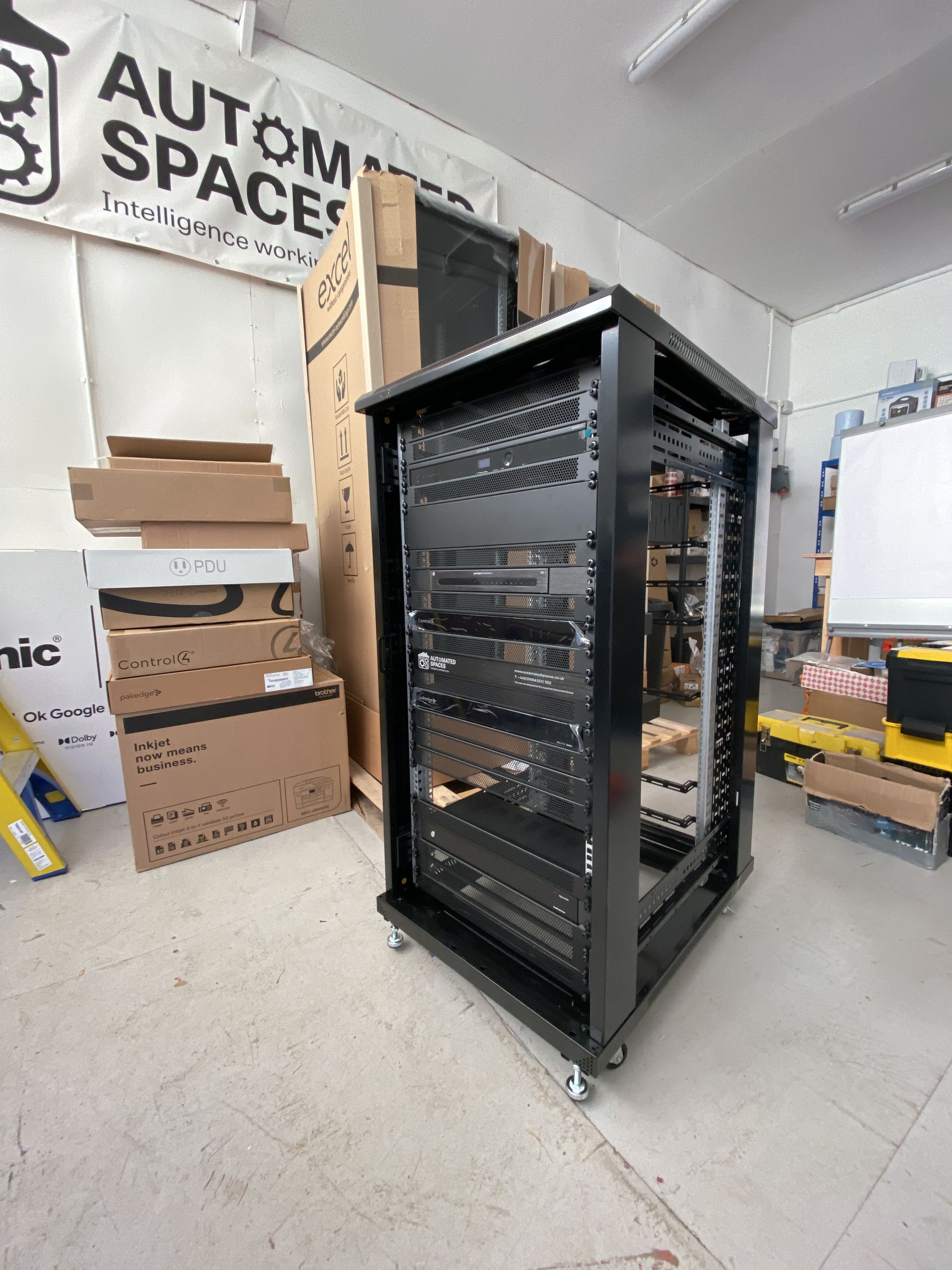 Black server rack on wheels in a warehouse with boxes and equipment.