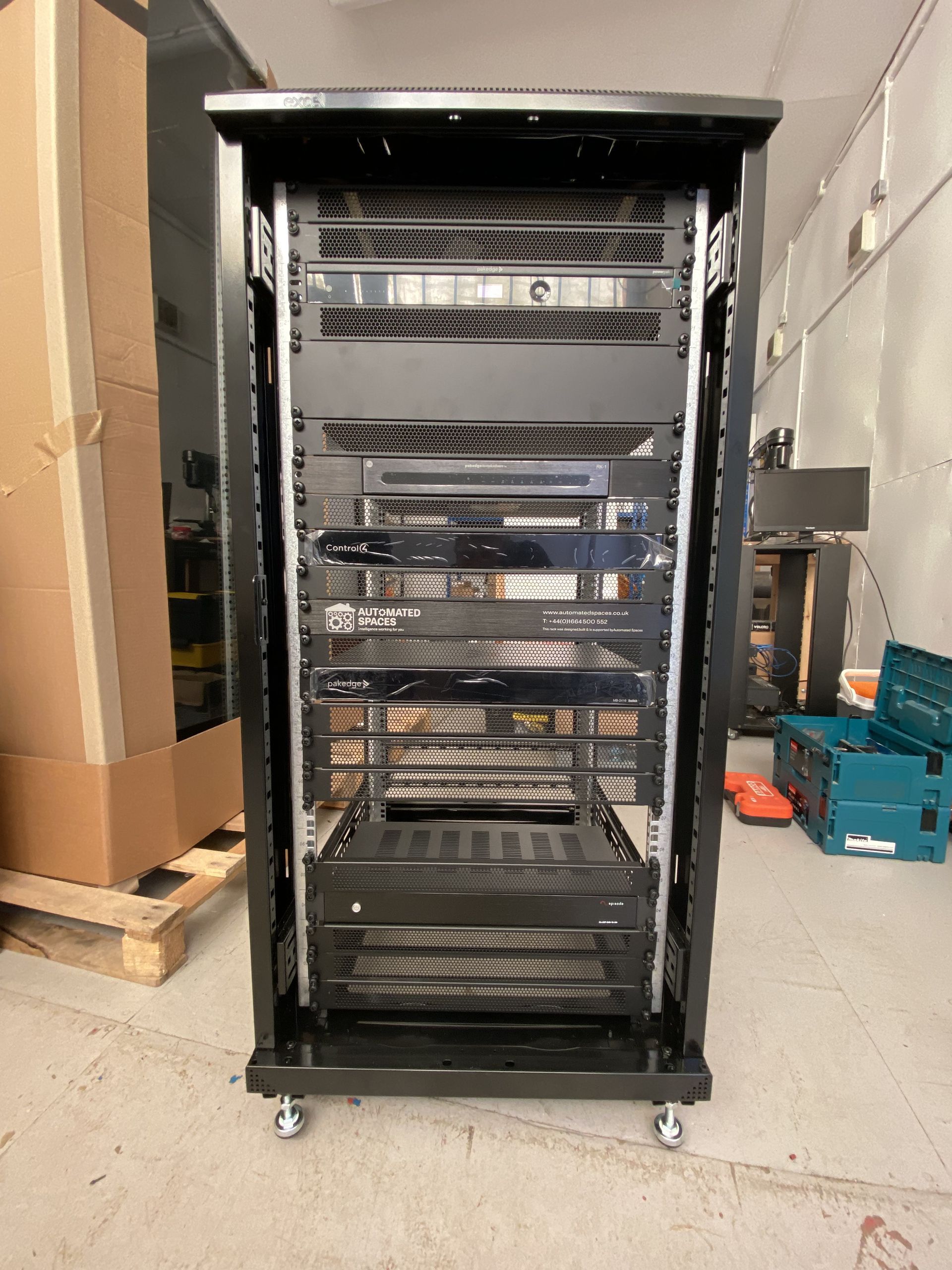 Black server rack on wheels, filled with electronic equipment, in a warehouse setting.