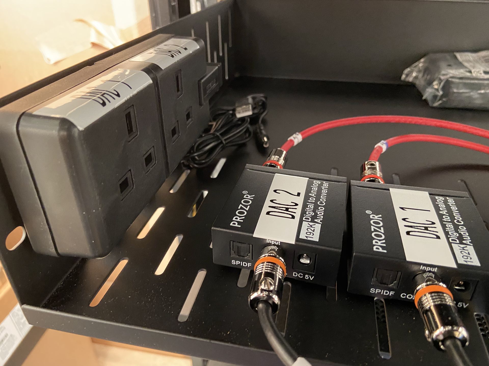 Black power strip and two black boxes with cables on a metal shelf.