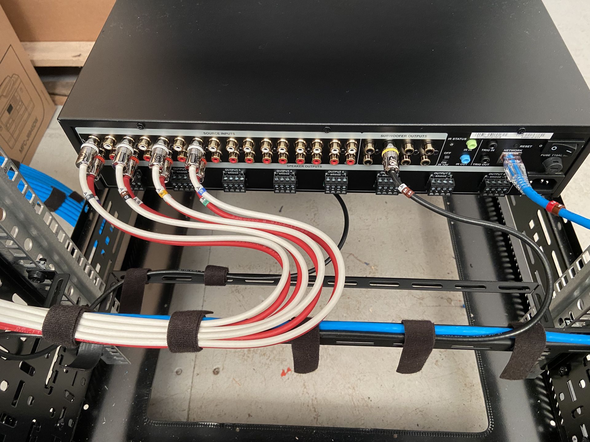 Black rack-mounted audio equipment with various colored cables connected, mounted inside a rack frame.