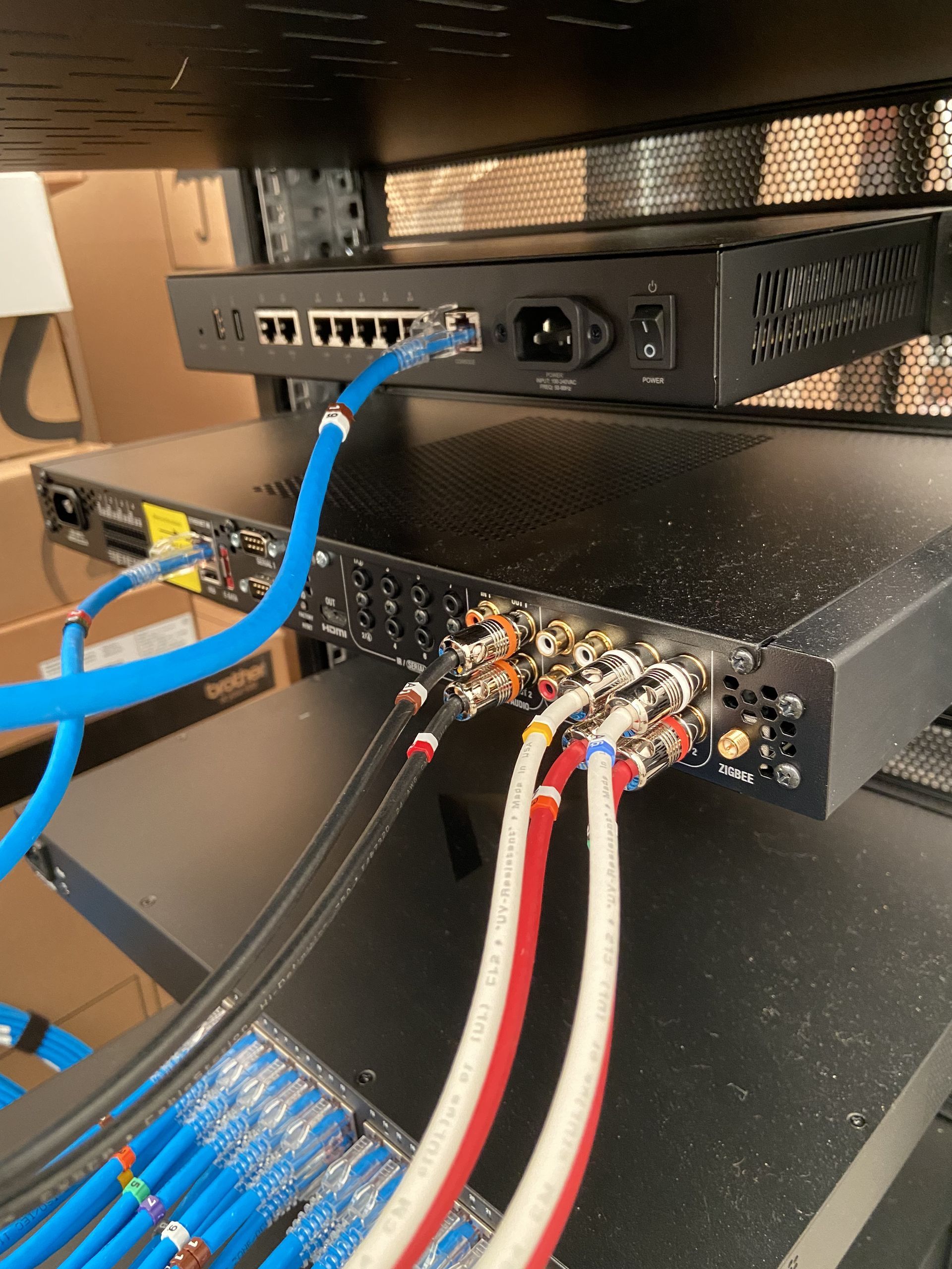 Rack-mounted electronics with blue, red, and white cables. Network switch above a receiver on a black shelf.