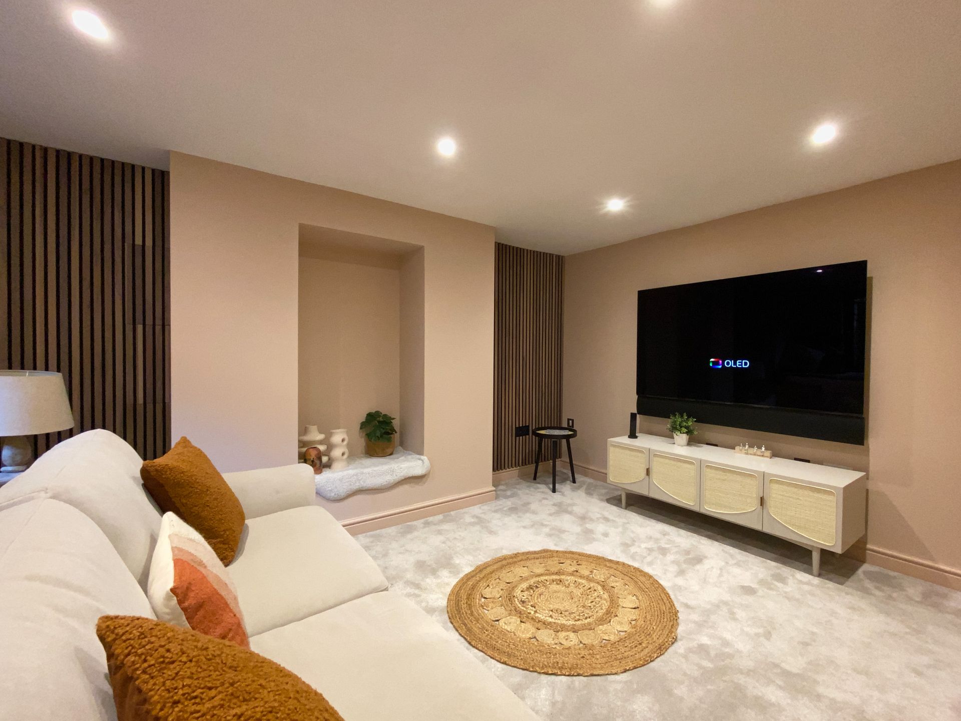 Cozy living room with neutral tones, a large TV, a sofa with orange pillows, and a circular rug.