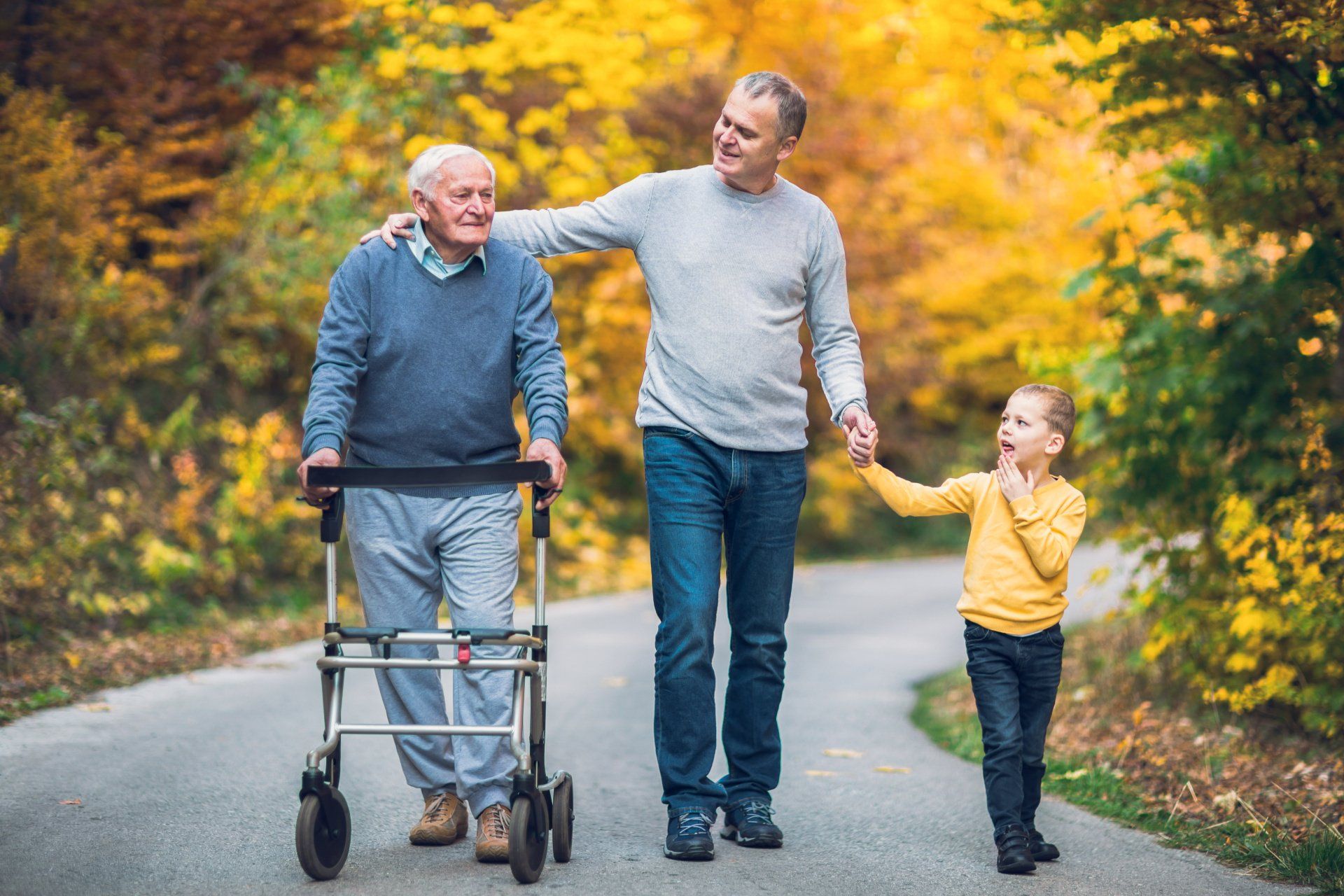 An old man with a walker, with a man and his son walking along a path together