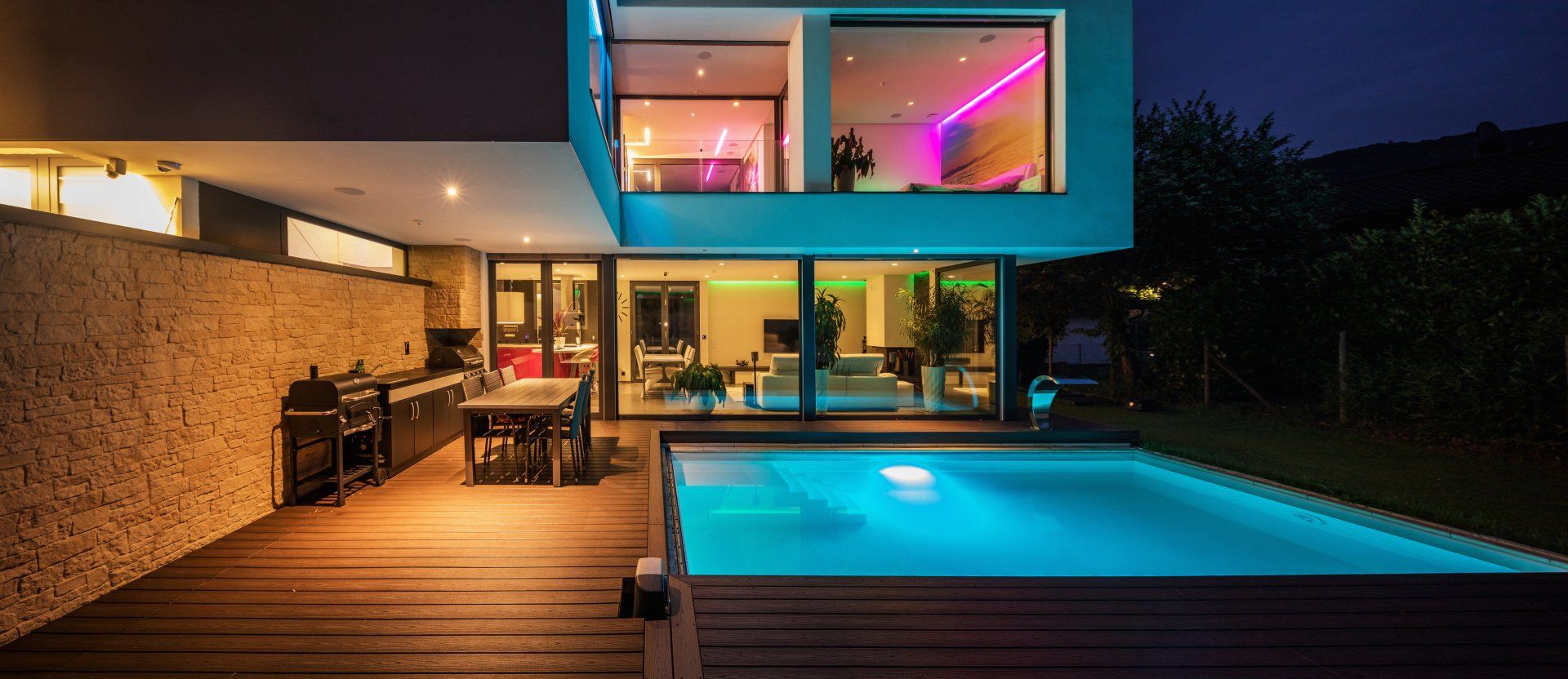 Modern home with a pool and colorful interior lights at night.