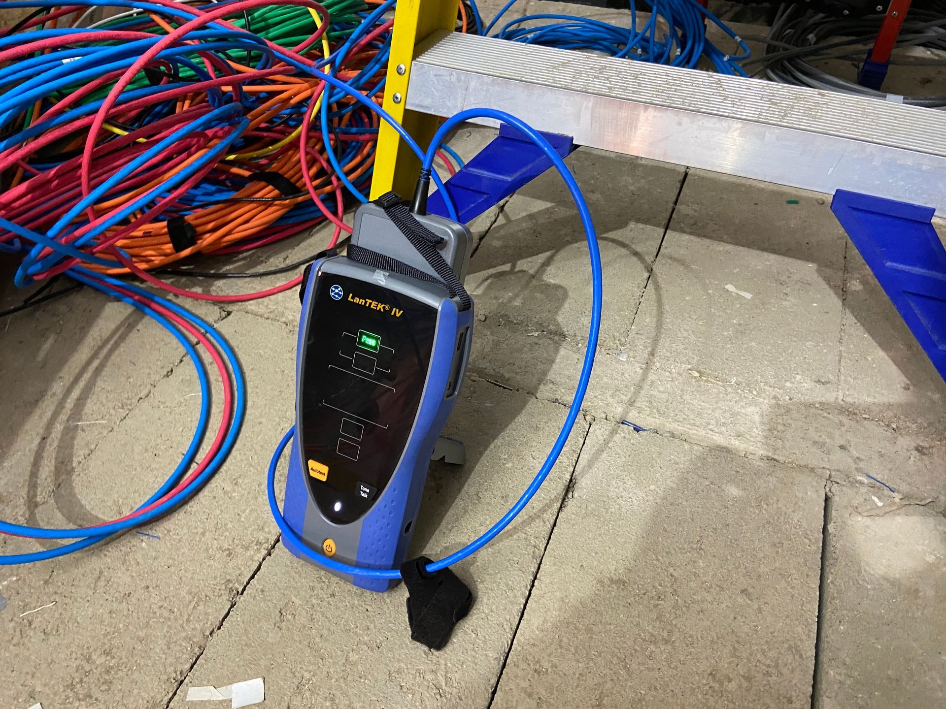 Blue portable electrical tester on a tiled floor beside coiled red and blue cables and a workbench