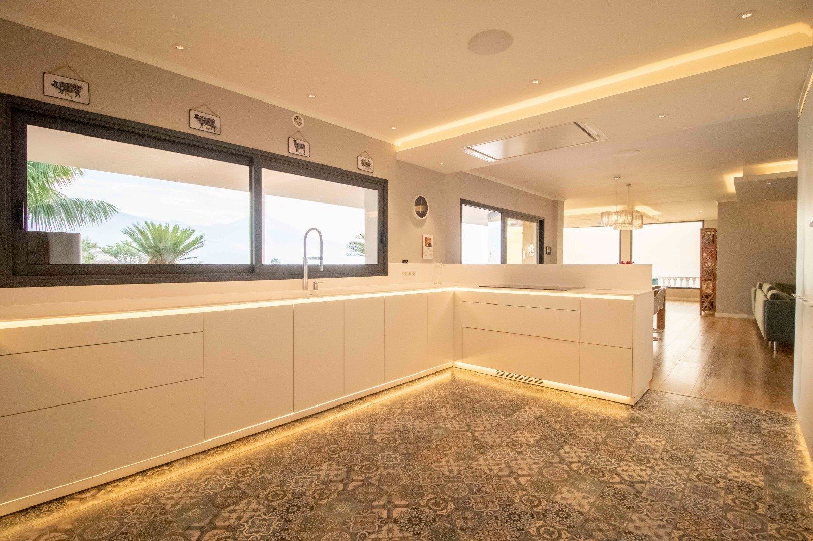 Modern white kitchen with under-cabinet lighting, large window, and hardwood floors.