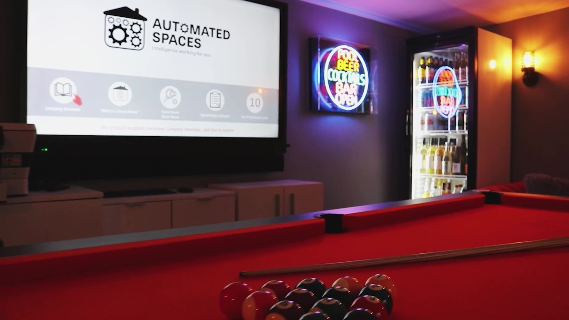 Pool table with a rack of balls, screen displaying “Automated Spaces,” and a neon sign.