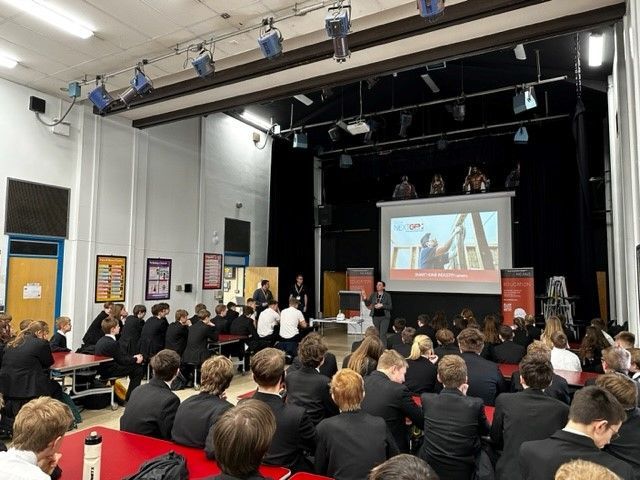 Photograph of a large hall filled with school students and a large projection screen showing CEDIA NextGen Presenation on it