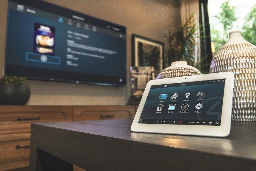 Control4 table top touch screen on a table in a room with a large TV in background displaying Control4 user interface