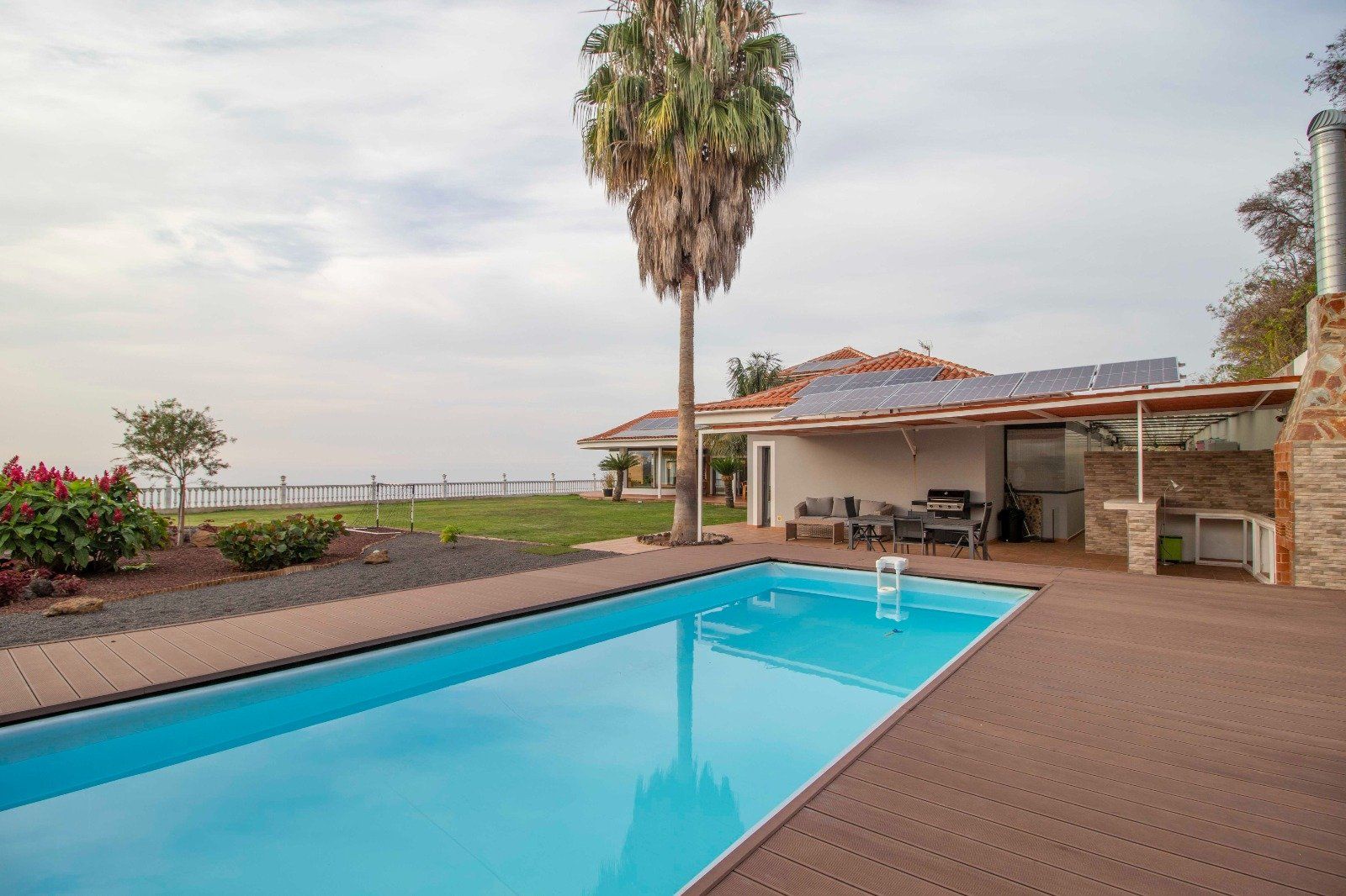 Swimming pool in a backyard with a view of the ocean, trees, and a small house.