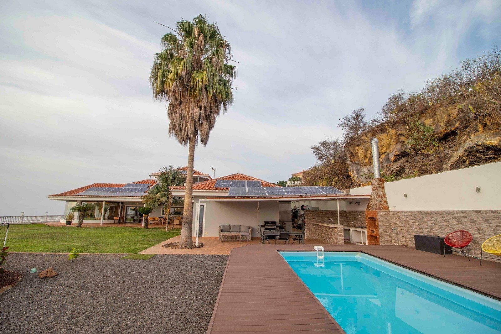 A home with a pool, palm tree, and solar panels, set against a hillside and ocean view.