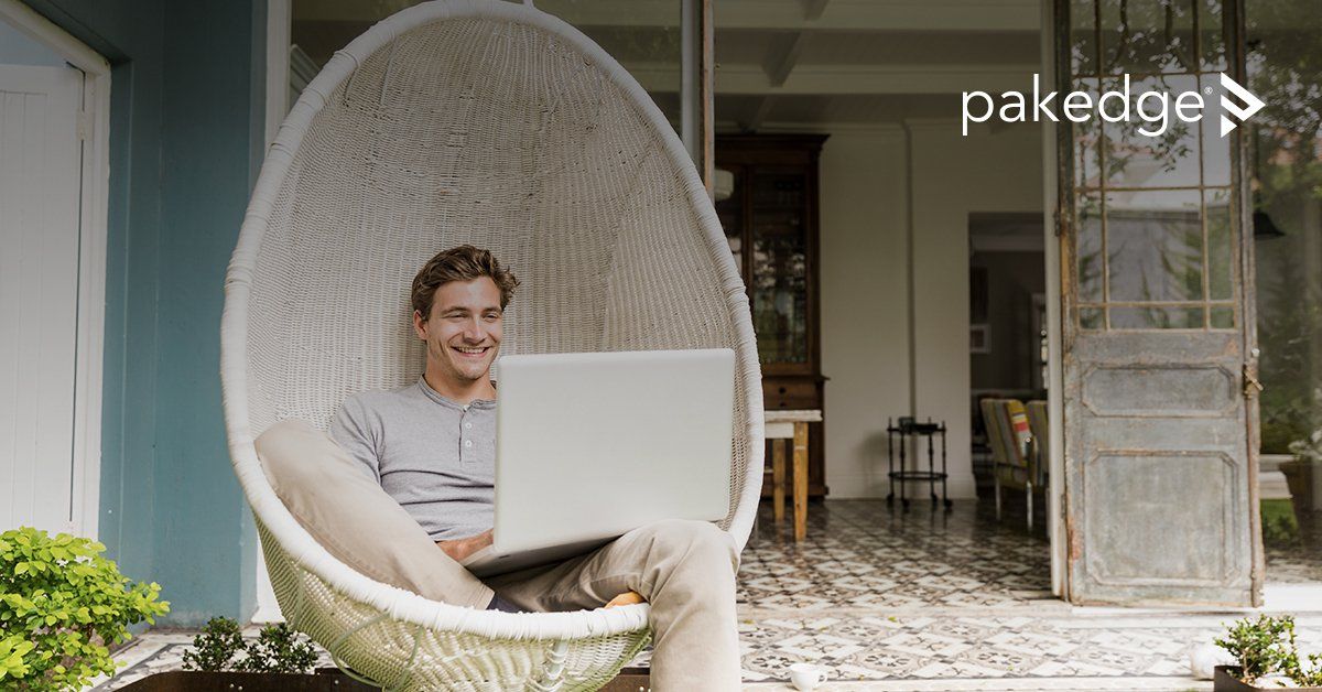 Man in hanging chair using a laptop on a porch, smiling at screen.
