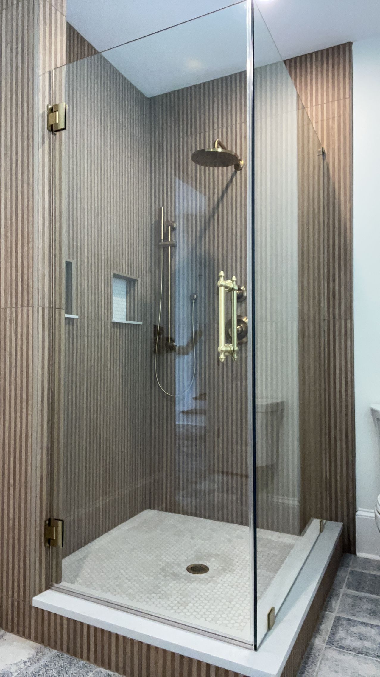 Modern glass shower enclosure with a white base and rainfall showerhead in a tiled bathroom