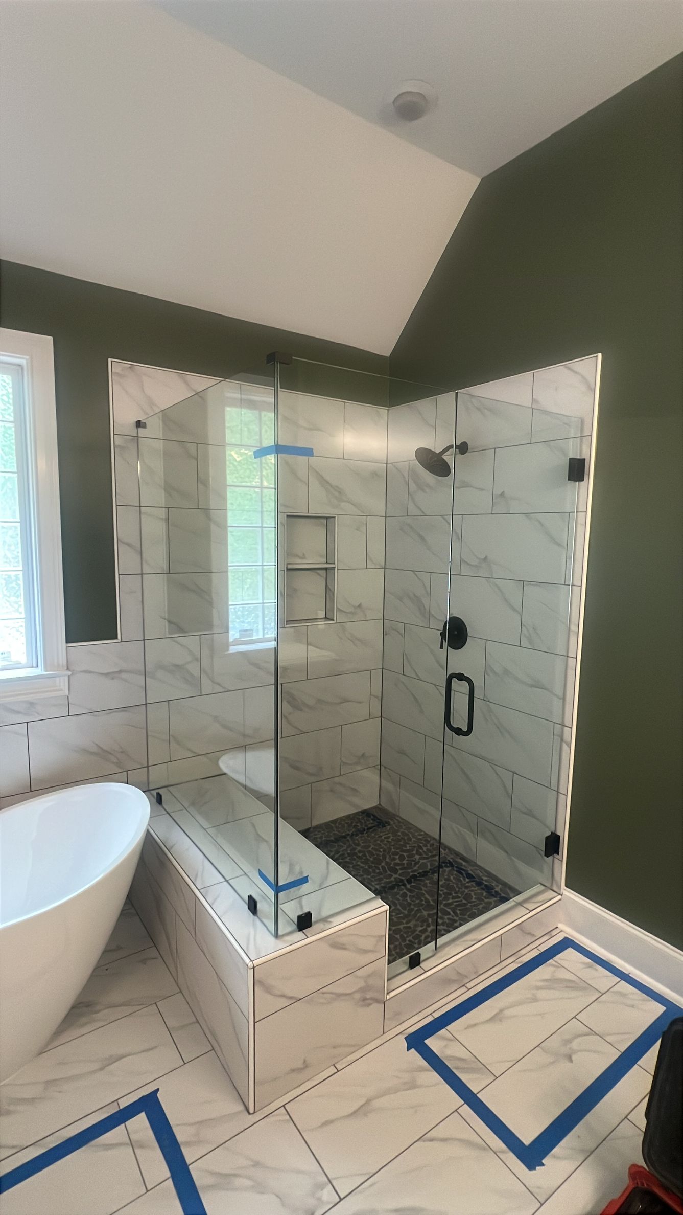Bright bathroom with freestanding tub, tiled shower, green walls, and two blue-taped floor openings