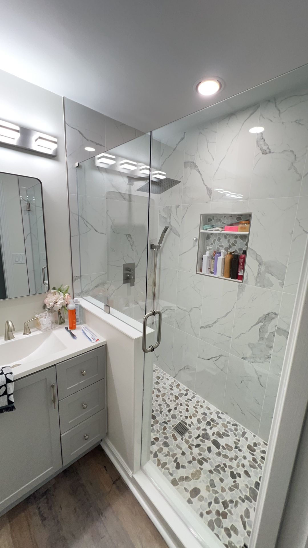 Modern white bathroom with vanity, glass shower, marble-pattern walls, and mosaic shower floor.