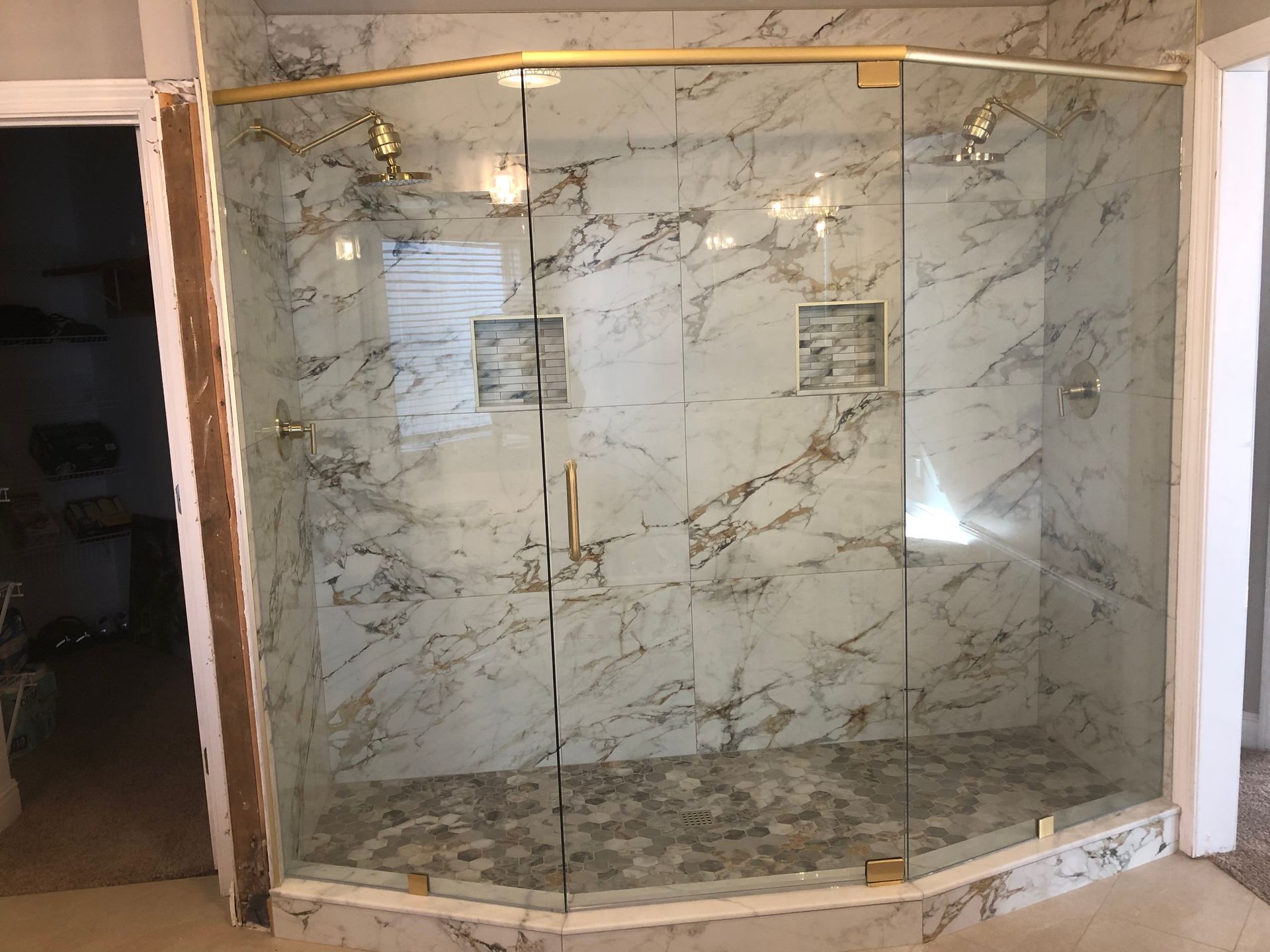 Curved glass shower enclosure with marble-look tile walls and gold trim in a bathroom
