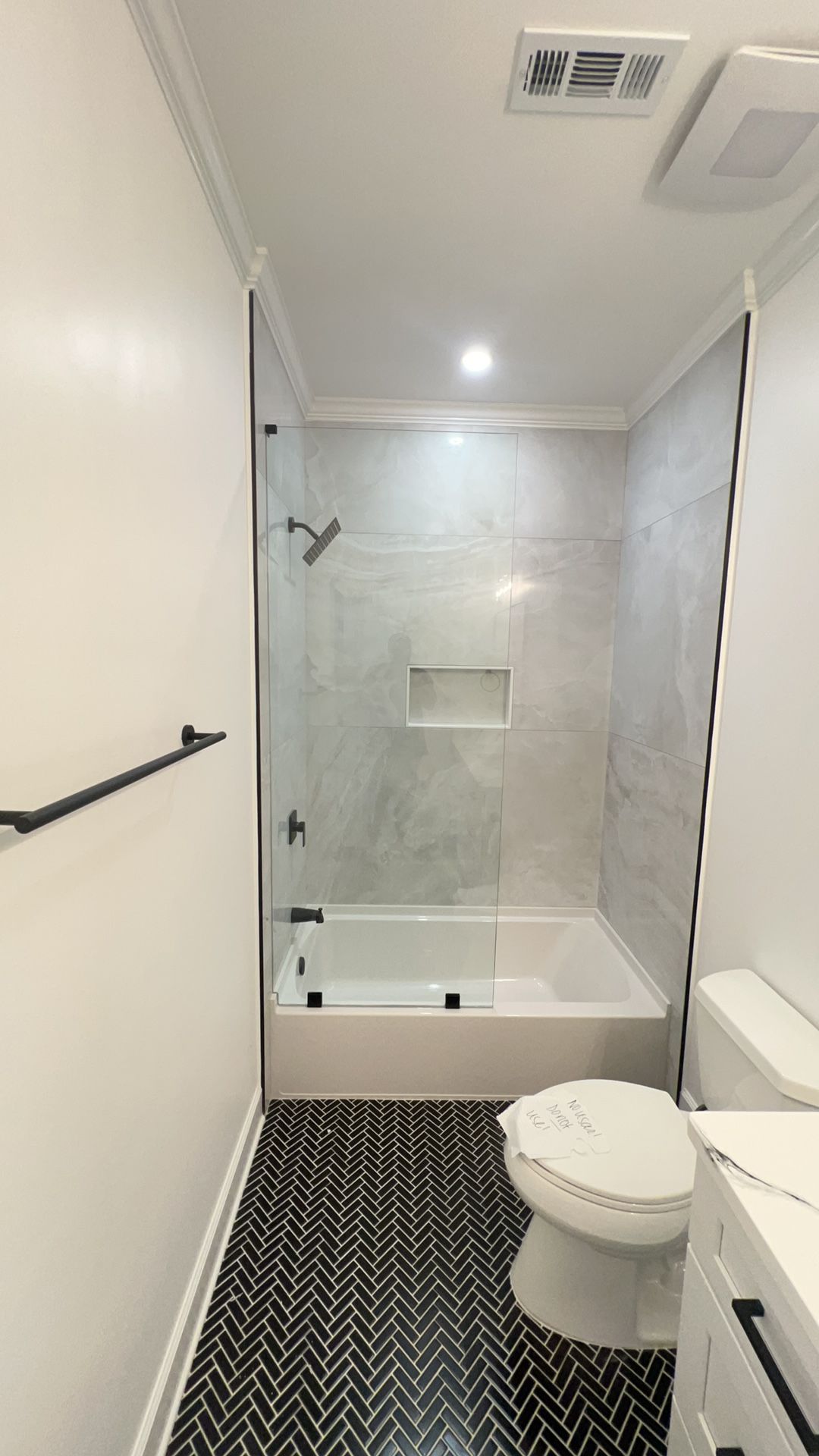 Small bathroom with white tub-shower, toilet, black-and-white patterned floor, and recessed ceiling light.