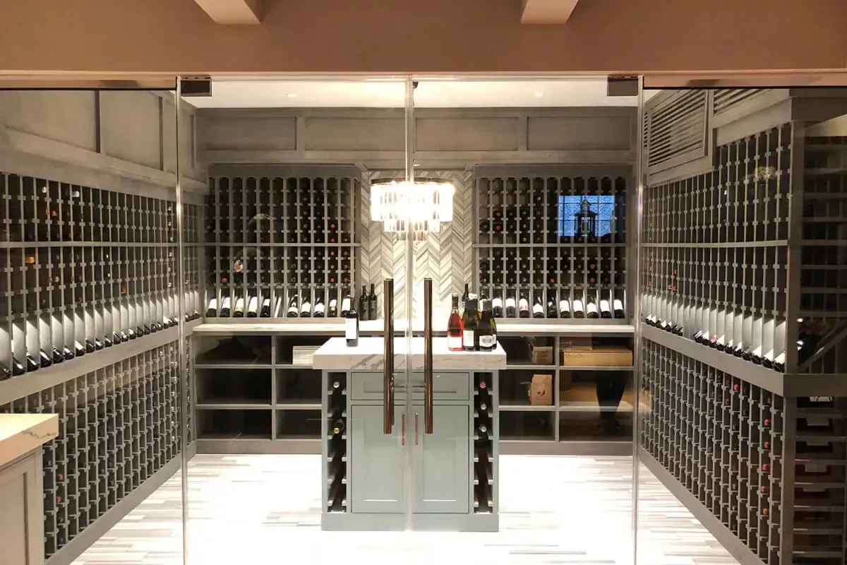 Wine cellar with glass doors, racks of wine bottles, and a central marble-topped island with bottles.