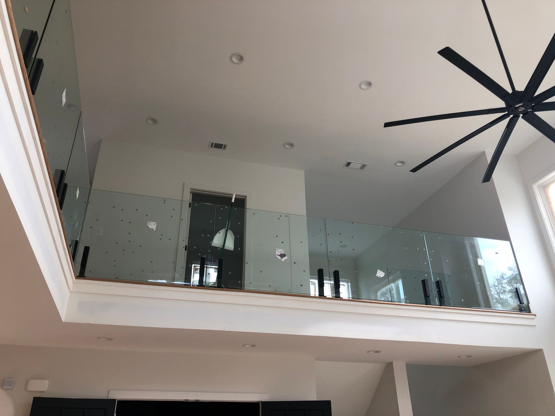 Modern living room with a mezzanine balcony, glass railing, recessed lights, and a large ceiling fan
