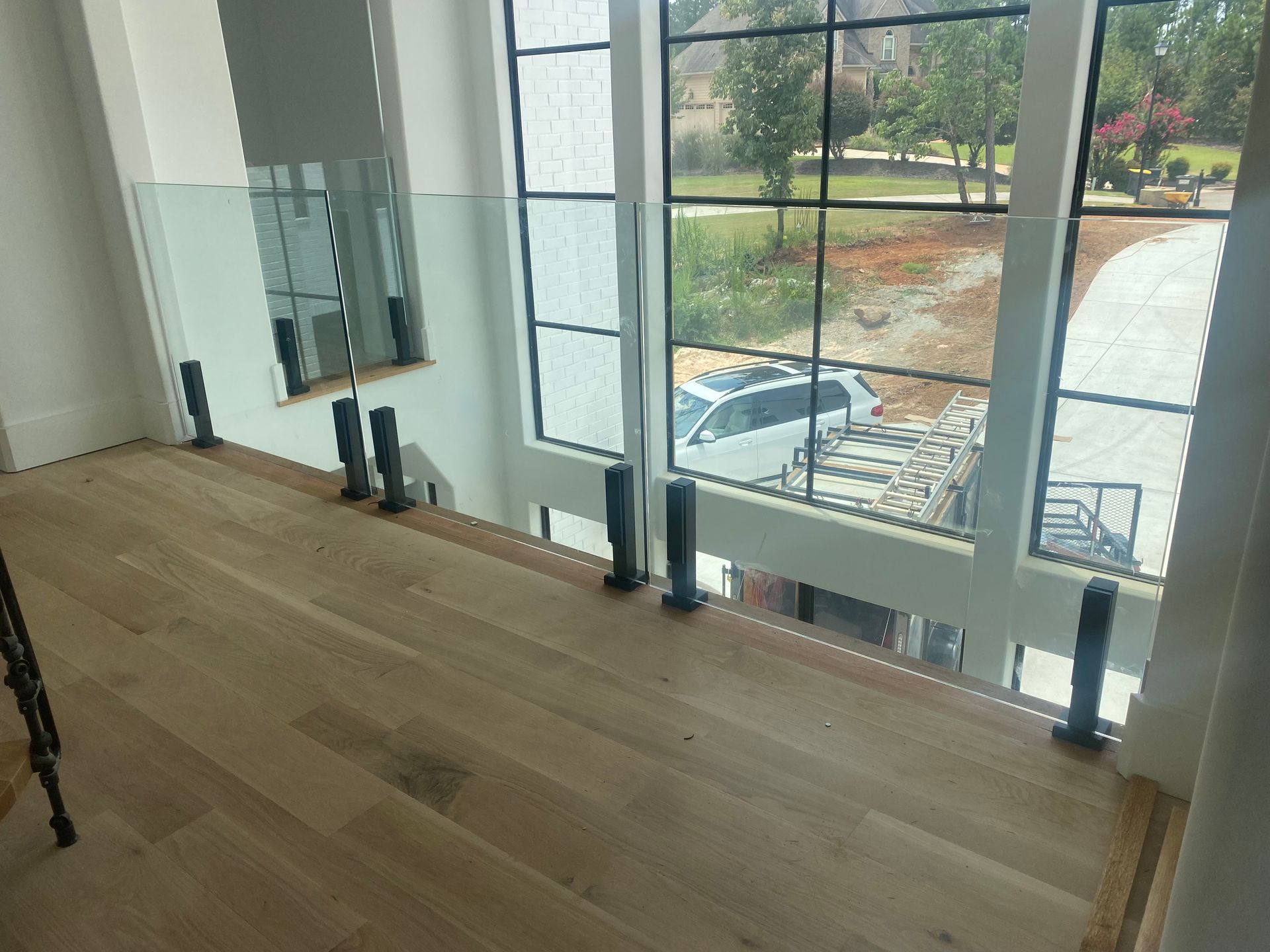 Empty wooden floor beside large windows overlooking a parking lot and trees