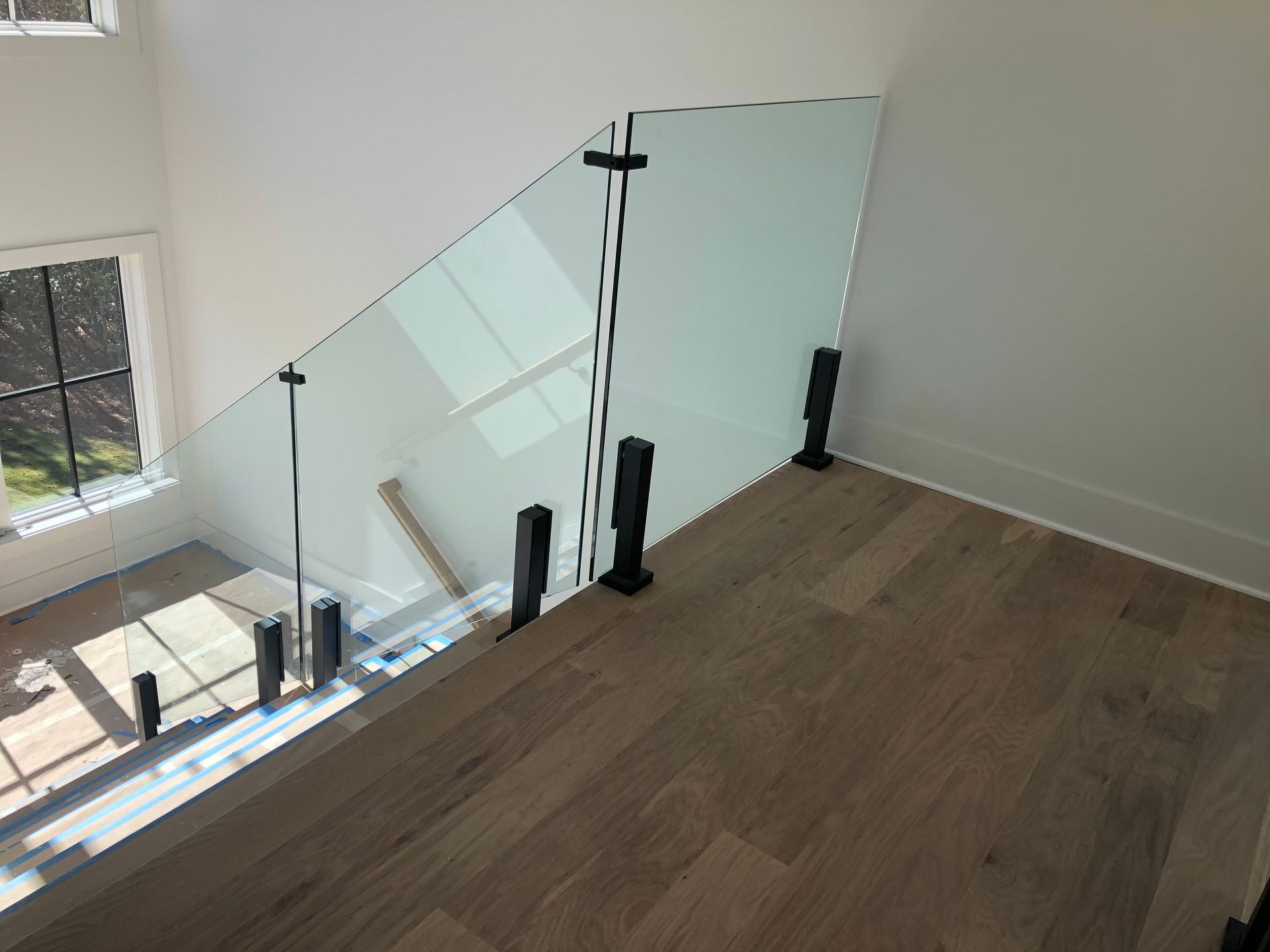Modern home interior with glass staircase railing and wood flooring near a window